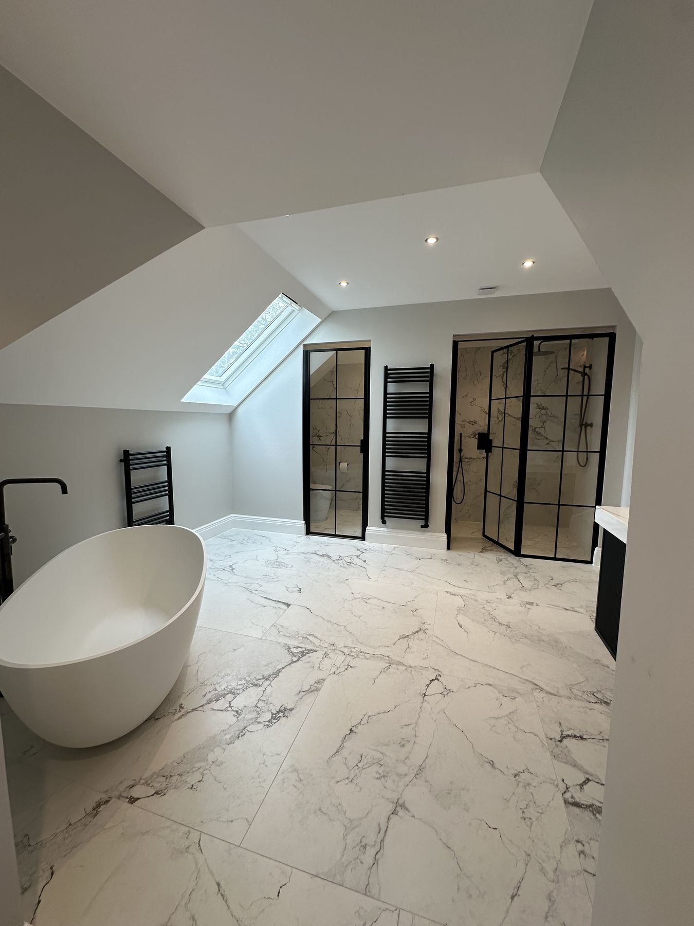 A finished loft master bathroom with a freestanding bath and black-framed screens