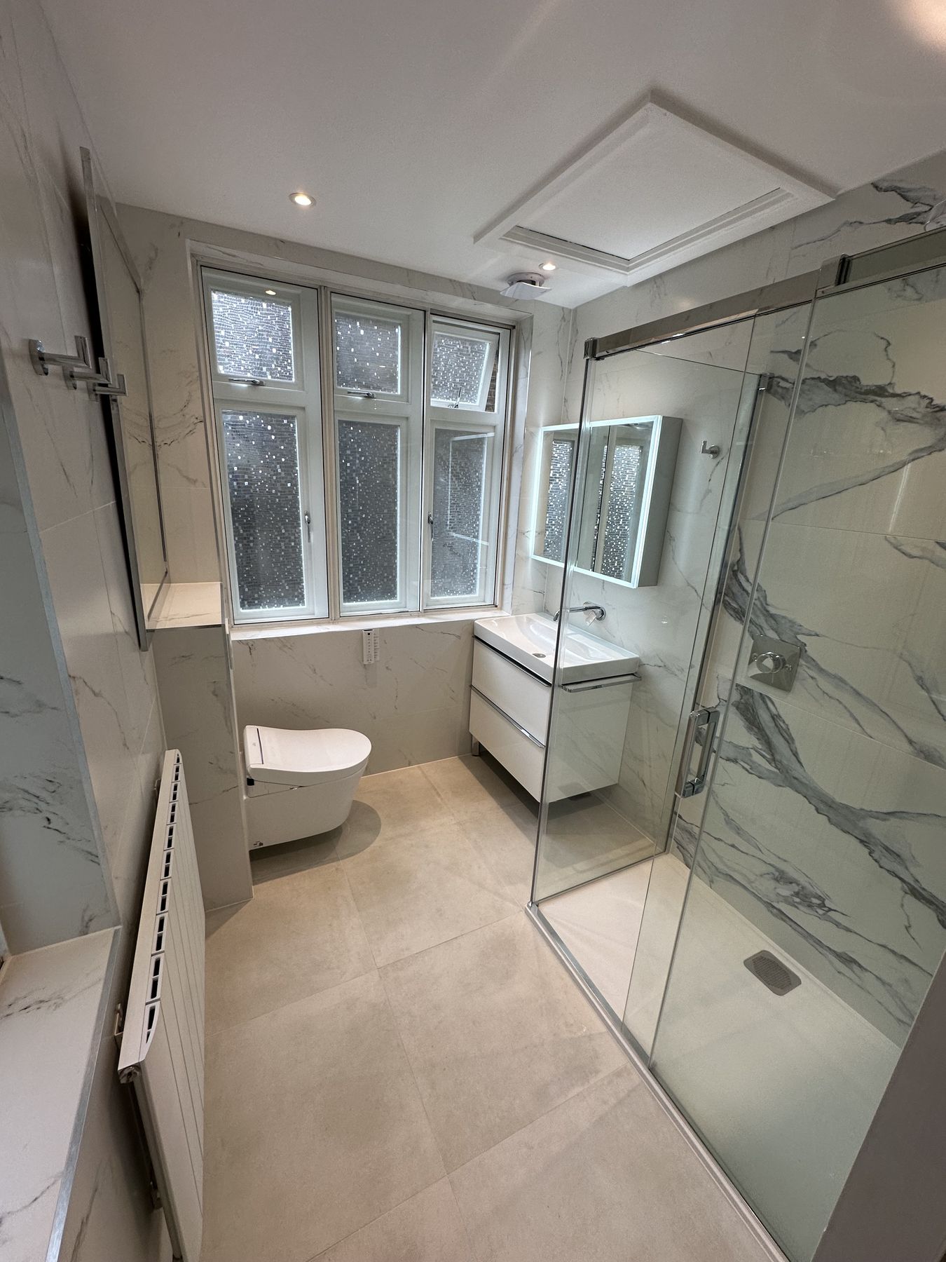 Marble-effect walk-in shower behind frameless glass beneath period windows
