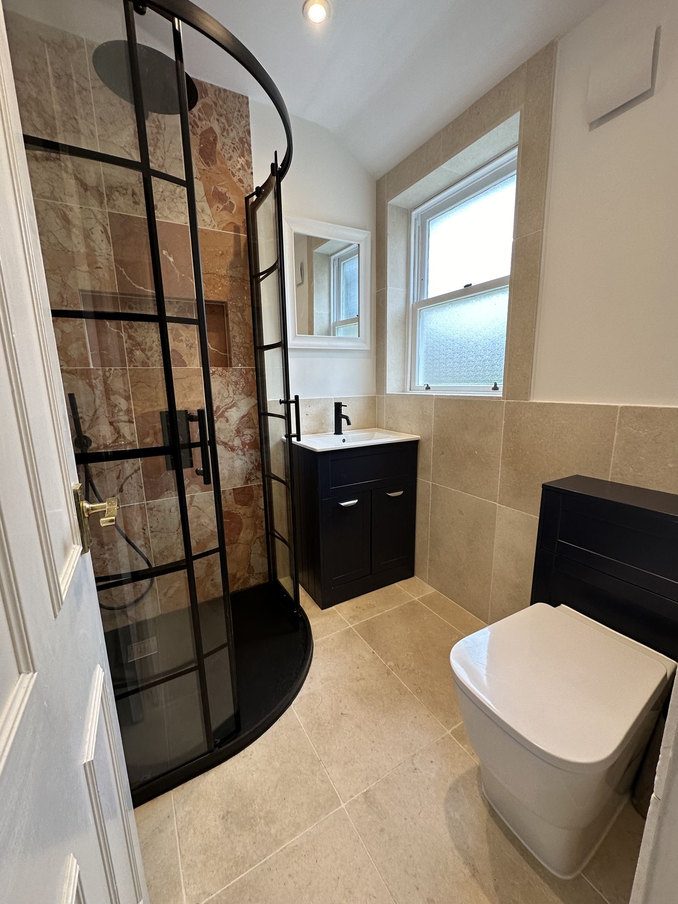 Shower room with rose marble walls and a curved black-framed enclosure
